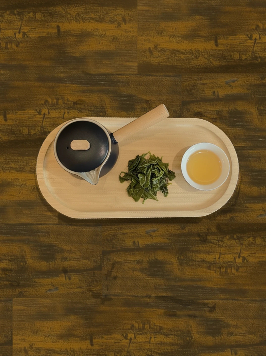 Overhead view of a tea tray with teapot, loose oolong leaves, and a cup of tea